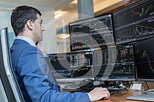 Stock broker trading online watching charts and data analyses on multiple computer screens.