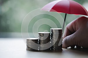 The stock of coins like a graph with blur background of a small red umbrella. The concept of coverage money