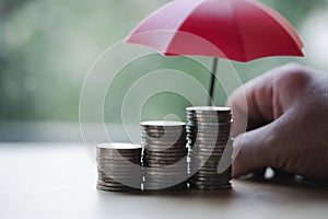 The stock of coins like a graph with blur background of a small red umbrella. The concept of coverage money