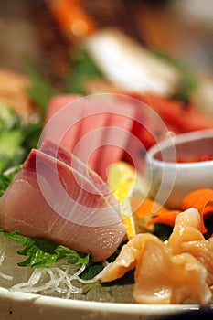 Stock image of a colorful platter of sashimi sushi with tuna and crab sticks in foreground and cucumber decorations