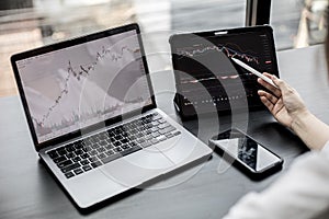 Stock investor holding a pen pointing a tablet screen that opens a stock chart program to read stock price charts.
