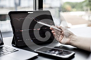 Stock investor holding a pen pointing a tablet screen that opens a stock chart program to read stock price charts.