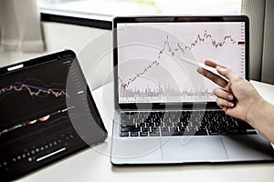 A stock investor holding a pen pointing to a laptop screen opens a stock chart program to read stock price charts.