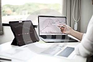 A stock investor holding a pen pointing to a laptop screen opens a stock chart program to read stock price charts.