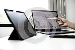 A stock investor holding a pen pointing to a laptop screen opens a stock chart program to read stock price charts.