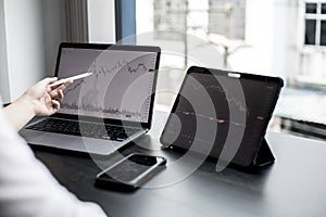 A stock investor holding a pen pointing to a laptop screen opens a stock chart program to read stock price charts.