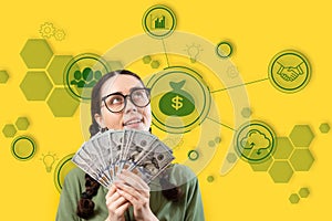 Stock market.Pretty smiling caucasian young woman wearing eyeglasses holding fan of dollar currency and looking up