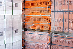 Stock pallets of red bricks wrapped in stretch film at wholesale outdoor market ot store. Construction site with prepared