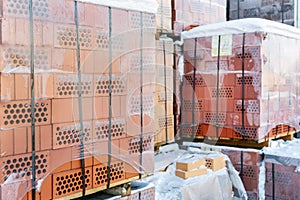 Stock pallets of red bricks wrapped in stretch film at wholesale outdoor market ot store. Construction site with prepared