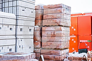 Stock pallets of red bricks wrapped in stretch film at wholesale outdoor market ot store. Construction site with prepared