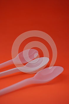 Stock photo of 3 stacks of white plastic spoons lined up and neatly arranged so that it looks aesthetic. Isolated on an orange