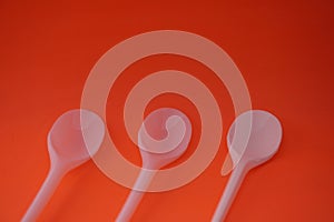 Stock photo of 3 stacks of white plastic spoons lined up and neatly arranged so that it looks aesthetic. Isolated on an orange