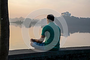 Stock photo of 30 to 40 year old Indian man practicing pranayama or yoga or meditation by the lake sitting in lotus pose at