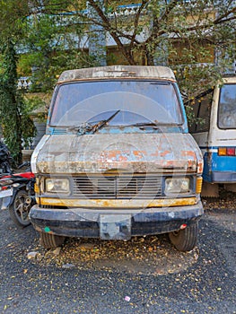 Stock photo of abandoned broken, damaged white color vans, motorcycle left in the scrap yard for recycling, green trees and