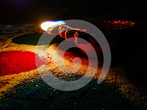 Stock photo of beautiful clay made oil lamp lit especially during diwali festival kept on colorful rangoli under dark background.