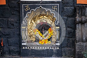 Stock photo of beautiful small temple of lord ganesha engraved on the wall painted with black color. clay made oil lamp near the