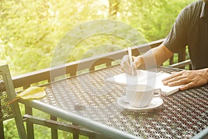 Stock photo :Coffee cup with closeup man writing a notebook on