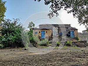 Stock photo of damaged, ruined Traditional red brick house with pyramid shape roof top in Indian village, surrounded by green tree