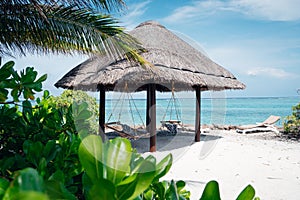 Stock photo features beach chairs with a woven hammock suspended above the water, Maldives