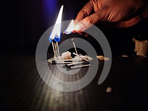 Stock photo of a human hand holding lighted matchsticks with yellow and blue color flame for lighting up the matchsticks which is