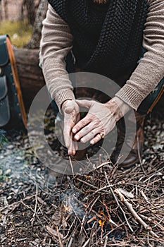 A stock photo of a man in nature sitting by a small fire, warming himself