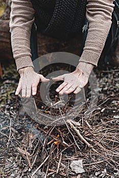 A stock photo of a man in nature sitting by a small fire, warming himself