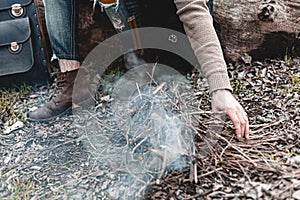 A stock photo of a man in nature sitting by a small fire, warming himself