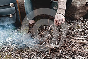 A stock photo of a man in nature sitting by a small fire, warming himself