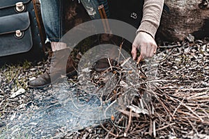 A stock photo of a man in nature sitting by a small fire, warming himself