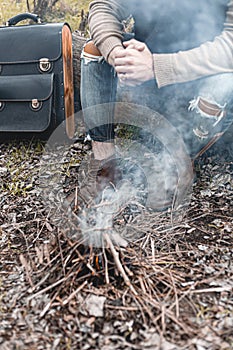 A stock photo of a man in nature sitting by a small fire, warming himself