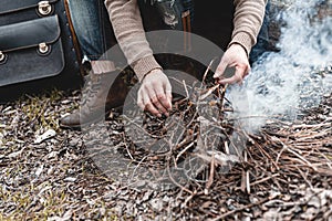 A stock photo of a man in nature sitting by a small fire, warming himself