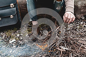 A stock photo of a man in nature sitting by a small fire, warming himself