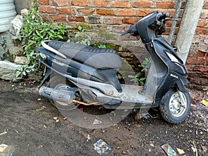 Stock photo old damaged black color suzuki access scooter, scooty or bike parked near the wall.