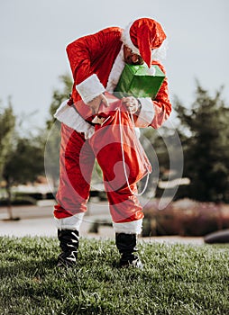 Stock photo of Santa Claus without beard standing putting presents in a red bag. Christmas time