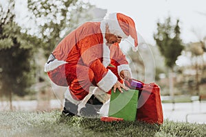 Stock photo of Santa Claus without beard standing putting presents in a red bag. Christmas time