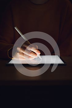 Stock photo of a woman`s hand writing on a tablet in the dark