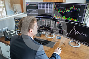 Stock trader looking at computer screens in trdading office.