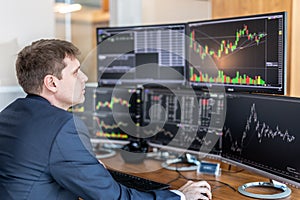 Stock trader looking at computer screens in trdading office.