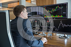 Stock trader looking at computer screens in trdading office.