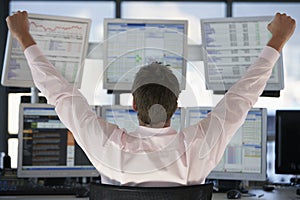 Stock Trader Watching Computer Screens With Hands Raised