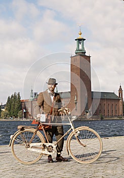 Man wearing old fashioned tweed suit and hat holding a retro bicycle in front of Stockholm City Hall
