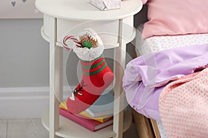 Stocking with presents hanging on white table in children`s room, closeup. Saint Nicholas Day tradition