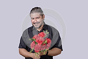 A stocky bearded man in a black polo shirt holding a bouquet of red roses. A single male in his 30s wooing and impressing a date. photo