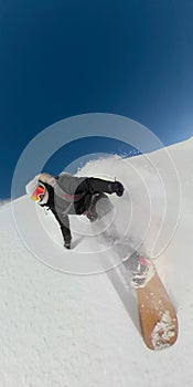 Stoked snowboarder girl carving off trail high in sunny mountains.