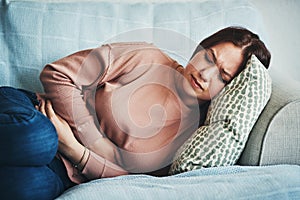 Stomach ache, pain and woman on home sofa with menstrual or period cramps in lounge. Sick, abdomen or colon problem of a