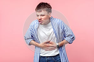 Stomach ache. Portrait of sick brown-haired man touching belly suffering abdominal pain. indoor, isolated on pink background