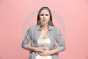 The stomach ache. The sad woman with stomach ache or pain on a pink studio background.