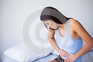 Stomach Pain. Unhealthy young woman with stomachache leaning on the bed at home