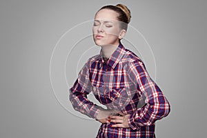 Stomack sick unhappy girl in red, pink checkered shirt, collected bun hairstyle, makeup standing and touching her painful belly