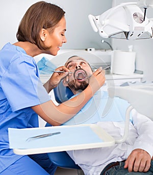 Stomatologist girl in uniform is taking visional inspection of a man